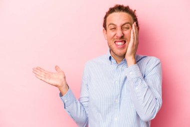 Pembe arka planda izole edilmiş genç beyaz bir adam avucunun içinde fotokopi alanı tutuyor, el üstünde tutuyor. Şaşırmış ve mutlu..