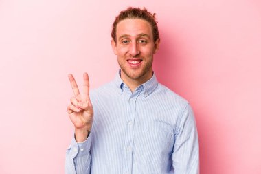 Pembe arka planda izole edilmiş genç beyaz adam zafer işareti gösteriyor ve gülümsüyor..