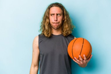 Mavi arka planda basketbol oynayan beyaz bir adam kafası karışmış, kendinden emin değil..