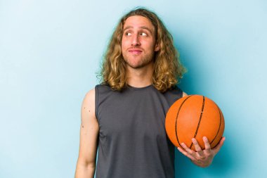 Basketbol oynayan beyaz bir adam mavi arka planda izole bir şekilde hedeflerine ve amaçlarına ulaşmayı hayal ediyor.
