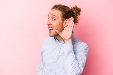 Pembe arka planda izole edilmiş genç beyaz adam bir dedikoduyu dinlemeye çalışıyor..