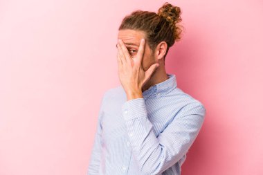Pembe arka planda izole edilmiş genç beyaz adam kameraya parmaklarıyla göz kırpıyor, yüzünü kapatmaktan utanıyor..