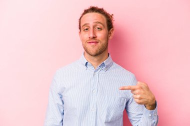 Pembe arka planda izole edilmiş genç beyaz bir adam gömlek fotokopi alanını elle gösteriyor, gururlu ve kendinden emin.