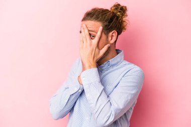 Pembe arka planda izole edilmiş genç beyaz adam parmaklarıyla gözünü kırp korkmuş ve gergin..