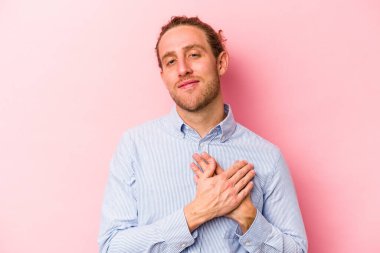 Pembe arka planda izole edilmiş genç beyaz bir adam, dostane bir ifadeye sahip, avuçlarını göğsüne bastırıyor. Aşk konsepti.