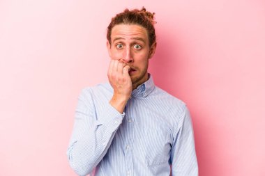 Pembe arka planda izole edilmiş, tırnak yiyen, gergin ve endişeli genç bir beyaz adam..