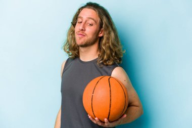 Mavi arka planda basketbol oynayan genç beyaz adam gülümseyen, neşeli ve keyifli görünüyor..