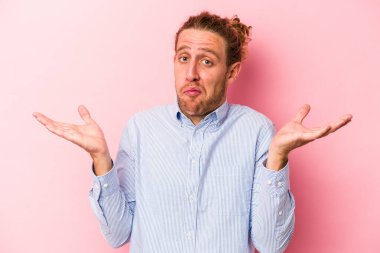 Pembe arka planda soyutlanmış genç beyaz bir adam sorgulama sırasında omuz silkiyor ve şüphe duyuyor..