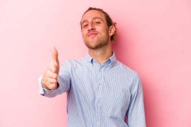 Pembe arka planda izole edilmiş genç beyaz adam selamlama jesti olarak kameraya elini uzatıyor..