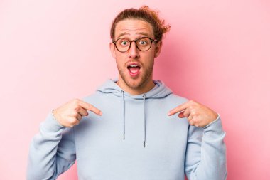 Pembe arka planda izole edilmiş genç beyaz adam parmağını göstererek şaşırdı, geniş bir gülümsemeyle..