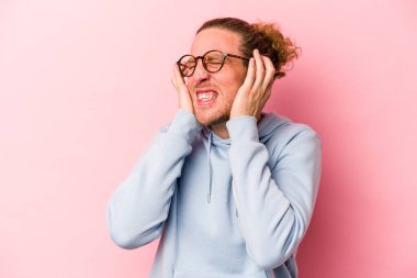 Pembe arka planda izole edilmiş genç beyaz adam kulaklarını elleriyle kapatıyor..