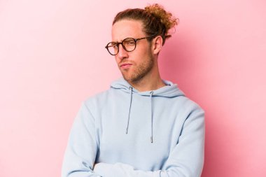 Pembe arka planda izole edilmiş genç beyaz adam şüpheli, belirsiz, seni muayene ediyor..