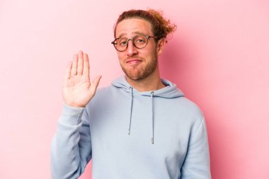 Pembe arka planda izole edilmiş genç beyaz adam gülümseyerek beş numarayı parmaklarıyla gösteriyor..