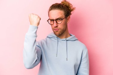 Pembe arka planda izole edilmiş genç beyaz adam yumruğunu kameraya gösteriyor, agresif yüz ifadesi var..