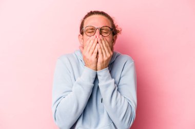 Pembe arka planda izole edilmiş genç beyaz bir adam bir şeye gülüyor, elleriyle ağzını kapatıyor..