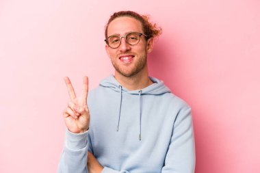 Pembe arka planda izole edilmiş genç beyaz adam iki numarayı parmaklarıyla gösteriyor..