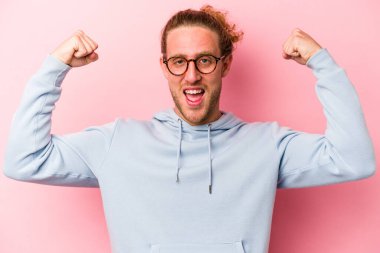 Pembe arka planda izole edilmiş genç beyaz bir adam güçlü bir hareket gösteriyor, kollarıyla, kadınsı gücün sembolü.