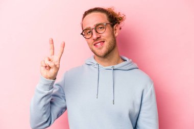 Genç beyaz adam pembe arka planda izole edilmiş neşeli ve kaygısız parmakları olan bir barış sembolü gösteriyor..