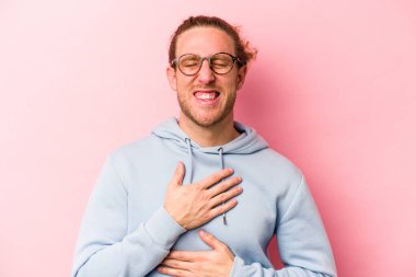 Pembe arka planda izole edilmiş genç beyaz adam mutlu bir şekilde gülüyor ve ellerini karnının üstünde tutarak eğleniyor..