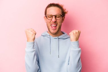 Pembe arka planda soyutlanmış, tasasız ve heyecanlı genç bir beyaz adam. Zafer konsepti.