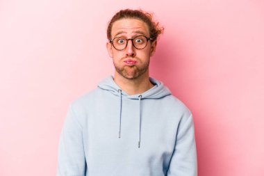 Pembe arka planda izole edilmiş genç beyaz adamın yanakları şişer, yorgun bir ifadesi vardır. Yüz ifadesi kavramı.