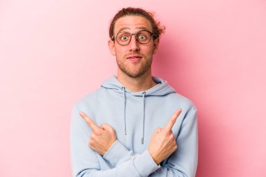 Pembe arka plan noktalarında izole edilmiş genç beyaz adam iki seçenek arasında seçim yapmaya çalışıyor..