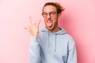 Pembe arka planda izole edilmiş genç beyaz adam parmaklarıyla taş hareketi gösteriyor.