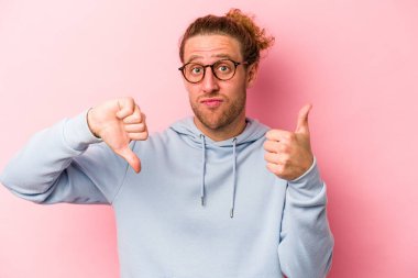 Pembe arka planda izole edilmiş genç beyaz bir adam baş parmağını kaldırıyor ve baş parmağıyla işaret ediyor. Zor bir seçim.
