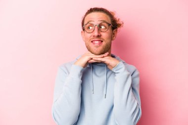 Pembe arka planda izole edilmiş genç beyaz adam ellerini çenesinin altında tutuyor, mutlu bir şekilde yana bakıyor..