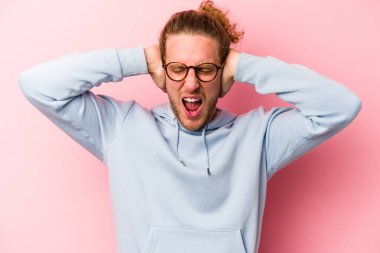 Kafkasyalı genç adam pembe arka planda izole edilmiş kulakları kulaklarıyla kapatıyor çok fazla ses duymamaya çalışıyor..