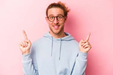 Pembe arka planda izole edilmiş genç beyaz adam iki parmağı da boş bir alan gösteriyor..