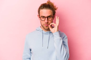 Pembe arka planda izole edilmiş genç beyaz bir adam parmakları dudaklarında bir sır saklıyor..