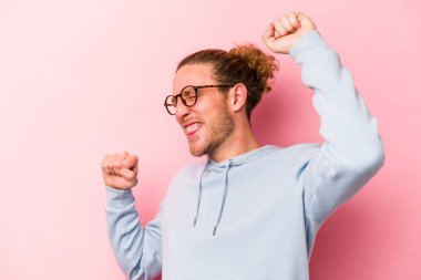 Pembe arka planda soyutlanmış genç beyaz adam özel bir günü kutluyor, atlıyor ve enerjiyle kollarını kaldırıyor..