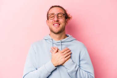 Pembe arka planda izole olmuş genç beyaz adam gülüyor, elini yüreğine koyuyor, mutluluk kavramını koruyor..