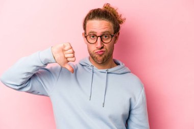 Pembe arka planda izole edilmiş genç beyaz adam baş parmağını aşağı gösteriyor, hayal kırıklığı konsepti..