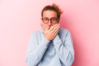 Pembe arka planda izole edilmiş genç beyaz adam elleri endişeli bir şekilde ağzı örtüyor..