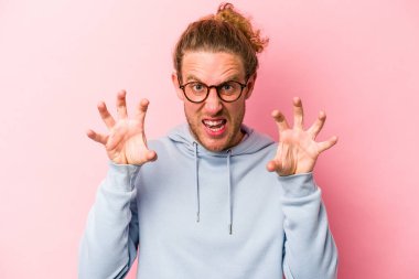 Pembe arka planda izole edilmiş genç beyaz adam pençelerini kedi taklidi yaparken gösteriyor, agresif bir hareket..