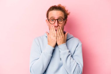 Pembe arka planda izole edilmiş genç beyaz adam şok olmuş, ağzı ellerle kaplanmış, yeni bir şey keşfetmeye hevesli..