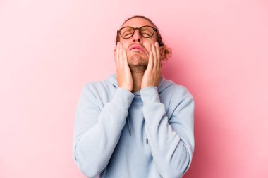 Kafkasyalı genç bir adam pembe arka planda izole edilmiş ağlıyordu, bir şeyden mutsuzdu, acı ve kafa karışıklığı içeriyordu..