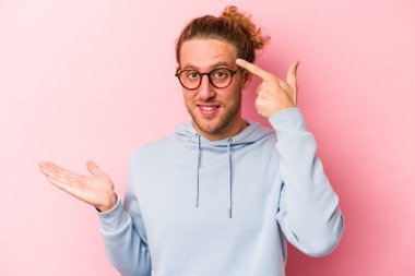 Pembe arka planda izole edilmiş genç beyaz adam elinde bir ürün tutuyor..