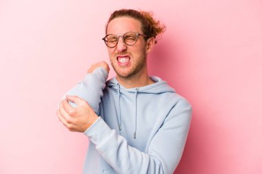 Genç beyaz adam pembe arka planda izole edilmiş dirsek masajı yapıyor, kötü bir hareketin ardından acı çekiyor..