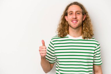 Beyaz arka planda izole edilmiş genç beyaz adam gülümsüyor ve başparmağını kaldırıyor.