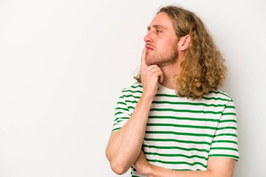 Beyaz arka planda izole edilmiş genç beyaz bir adam şüpheli ve şüpheci bir ifadeyle yana bakıyor..