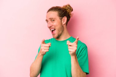 Pembe arka planda izole edilmiş genç beyaz adam parmaklarıyla ön tarafı işaret ediyor..