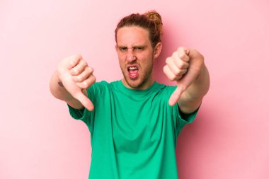Pembe arka planda izole edilmiş genç beyaz adam baş parmağını aşağı gösteriyor ve hoşlanmadığını ifade ediyor..
