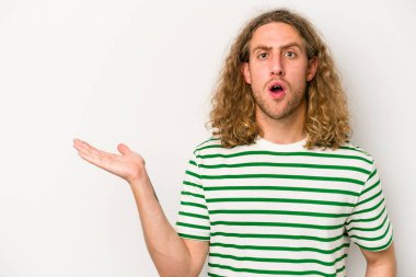 Beyaz arka planda izole edilmiş genç beyaz adam, avuç içi fotokopi alanını elinde tutmaktan etkilenmiş..