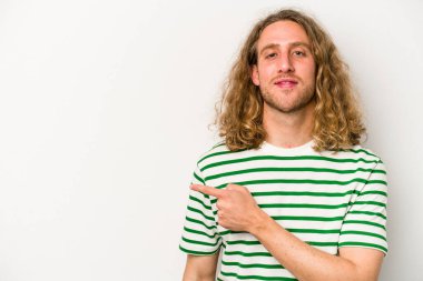 Beyaz arka planda izole edilmiş genç beyaz bir adam gülümsüyor ve boş alanda bir şeyler gösteriyor..