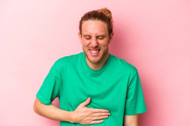 Pembe arka planda izole edilmiş genç beyaz adam karnına dokunuyor, nazikçe gülümsüyor, yemek yiyor ve tatmin oluyor..