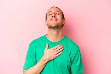 Pembe arka planda izole edilmiş genç beyaz adam yüksek sesle gülüyor elini göğsünde tutuyor..