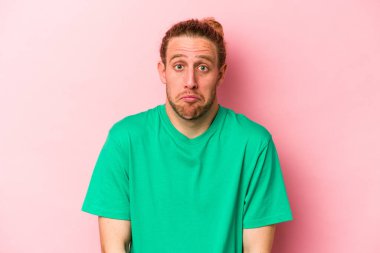 Pembe arka planda izole edilmiş genç beyaz adam omuzlarını silkeliyor ve gözleri açık..